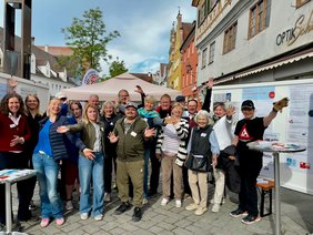 Eine große Gruppe von Menschen am Aktionsstand vor dem Freiheitsbrunnen. Sie werfen vor Freude die Arme in die Luft. 