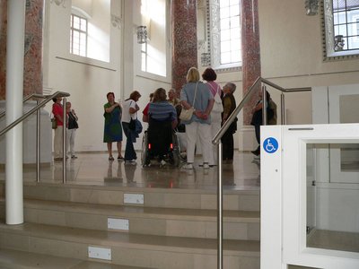 Gruppe mit Rollstuhlfahrerin im Kreuzherrensaal, im Vordergrund die Hebebühne, welche die Stufen überbrückt.