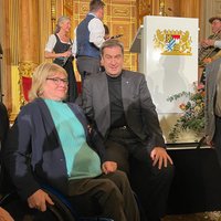 Auf dem Foto sitzt vor der Bühne Harald Güller neben Frau Gotzes. In der Mitte sitzt Ministerpräsident Markus Söder. Rechts steht Herman Wetzel aus Memmingen. Im Hintergrund sieht man Musikanten in Tracht, die am Abend auftraten. 