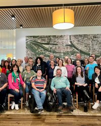 Die Teilnehmenden stehen, bzw. sitzen vor einer großen Luftbildaufnahme von Regensburg. 