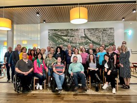 Die Teilnehmenden stehen, bzw. sitzen vor einer großen Luftbildaufnahme von Regensburg. 